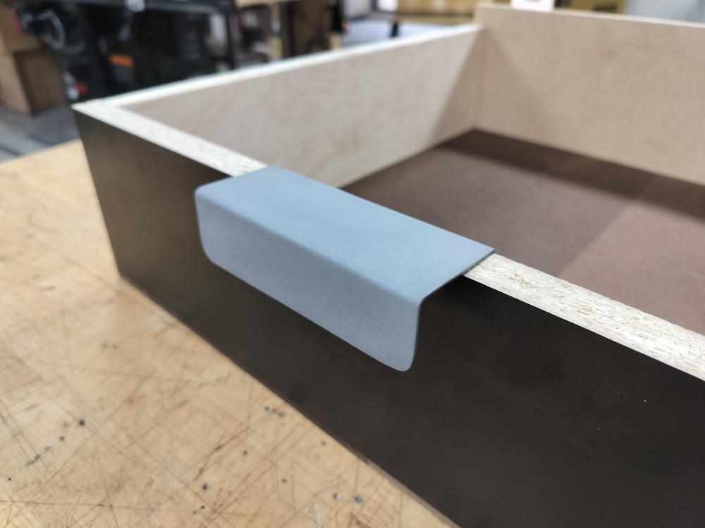 Bent sheet metal handle with sandblasted finish attached to face of drawer.