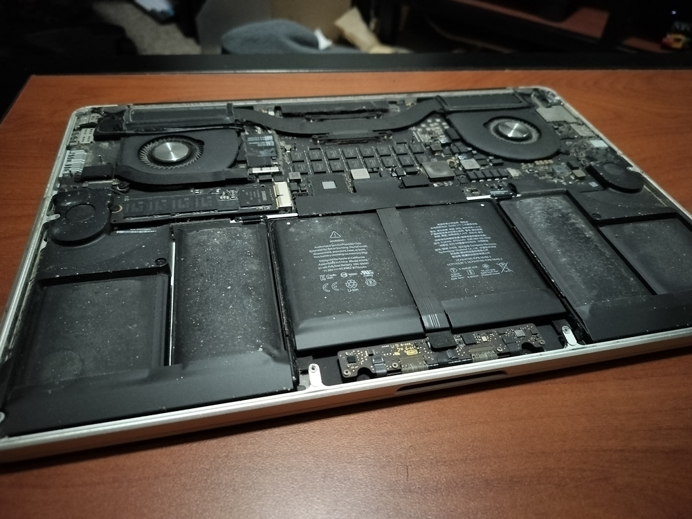 Insides of a mid 2015 A1398 MacBook Pro filled with dust, dirt, and a swollen battery.