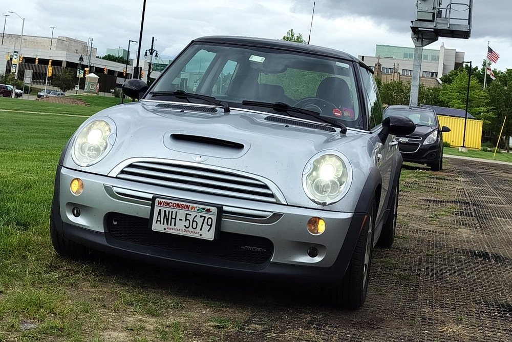 2006 Mini Cooper S front shot with lights on against gray sky.